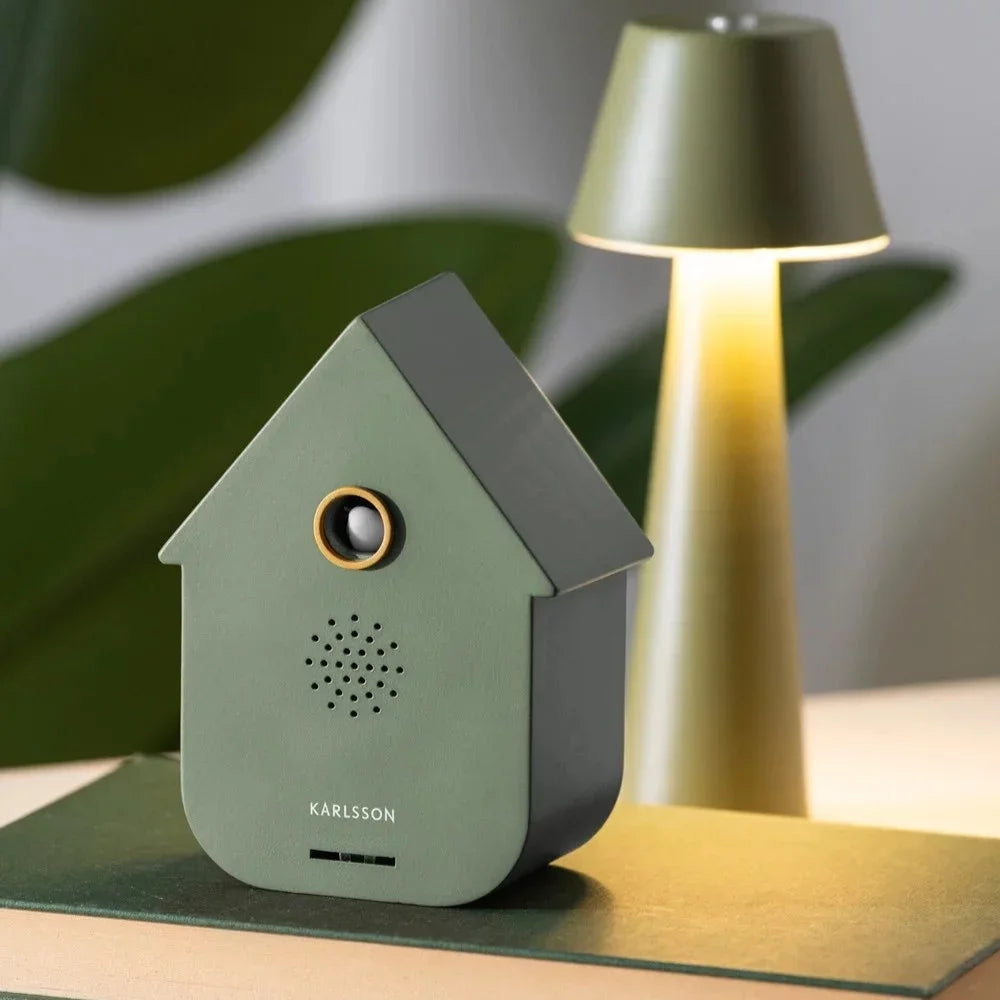  Groene Karlsson Modern Cuckoo sfeerbox decoratief geplaatst op een boek naast een brandende lamp
