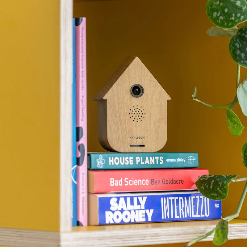 Karlsson Modern Cuckoo sfeerbox in lichte houtlook decoratief geplaatst op boeken in een kast.